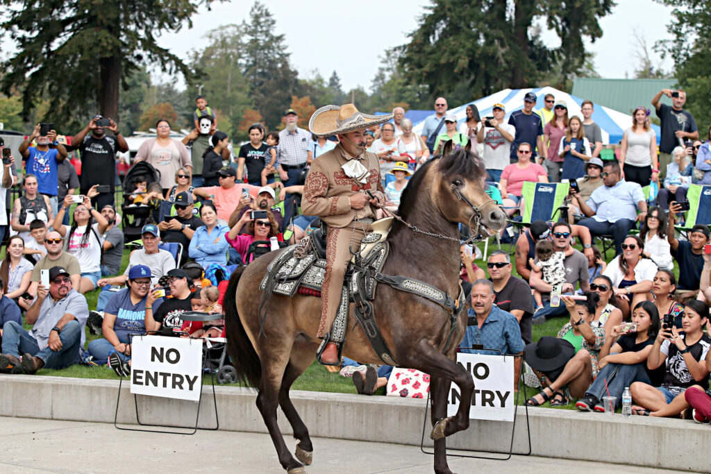 A person rides a horse during a performance on the paver area of The Pavilion at Fort Steilacoom Park while people sit on the grass watching.