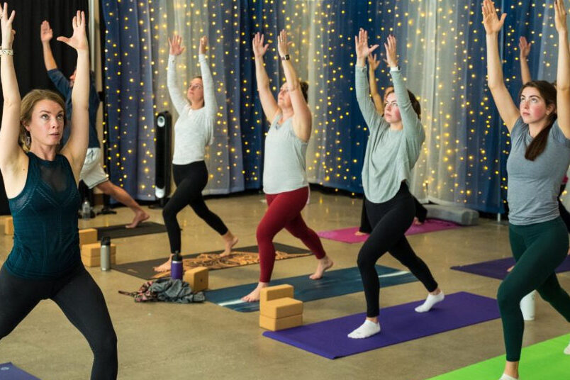 People stand with their arms in the air holding a yoga pose.