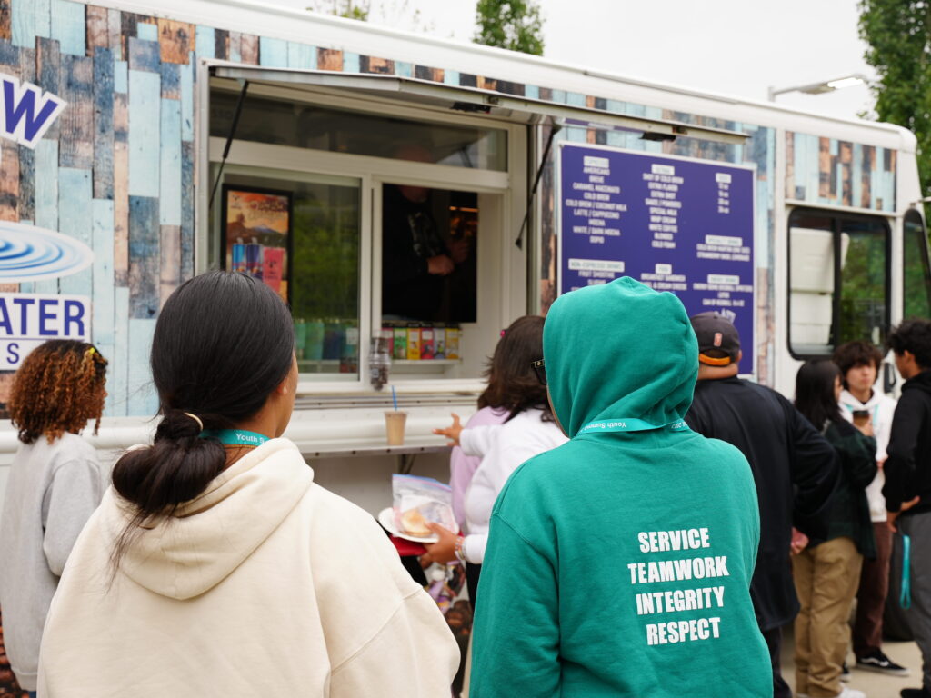A group of teens wait in line at a food truck.