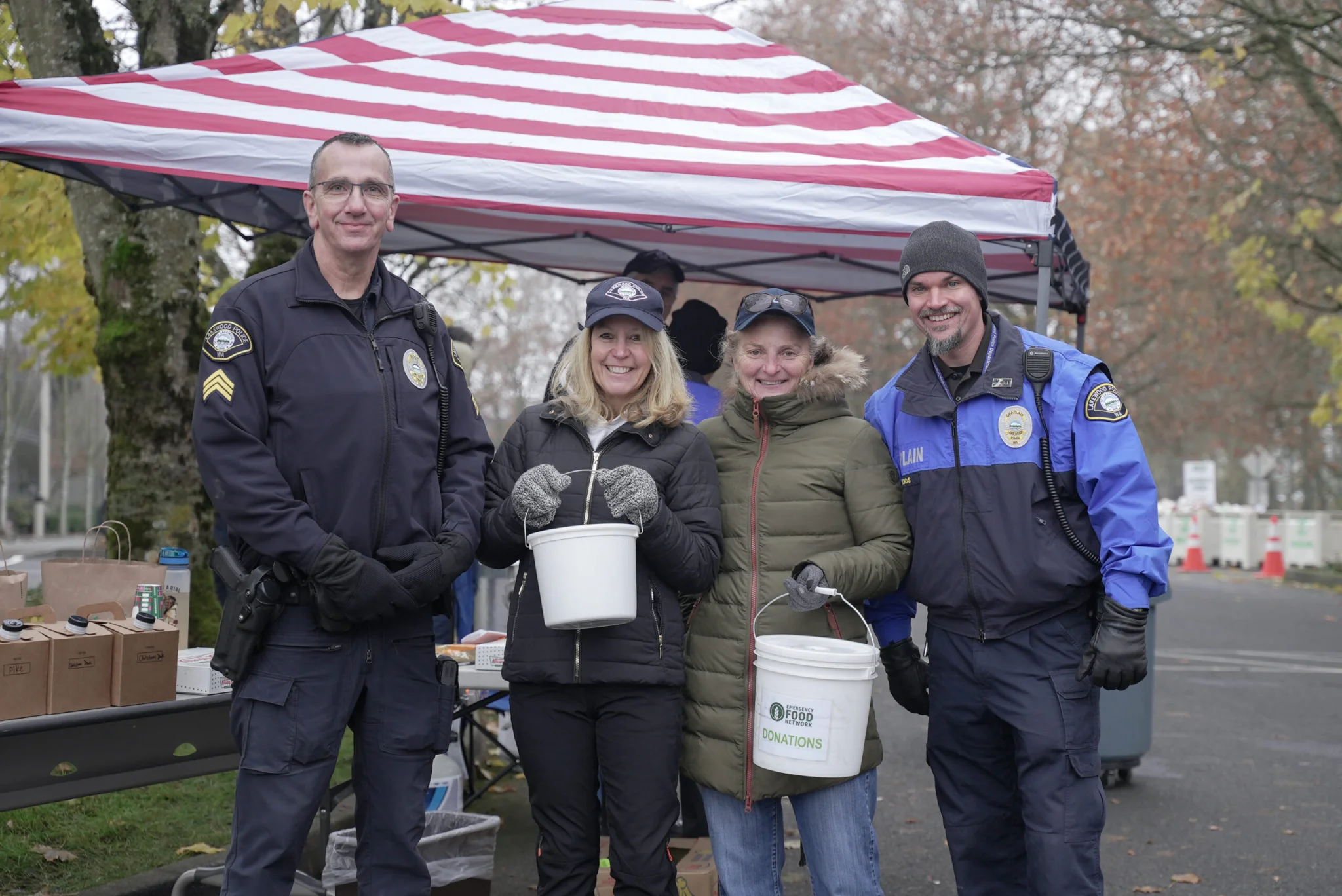 Four people stand side-by-side and smile for the camera. The two women in the middle are holding donation buckets.