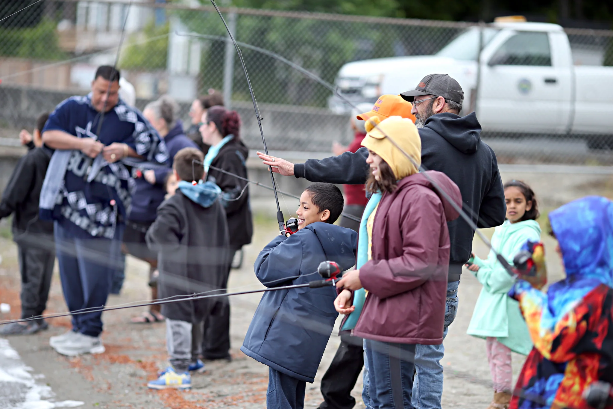 People line the beach with fishing poles all focused on catching fish.