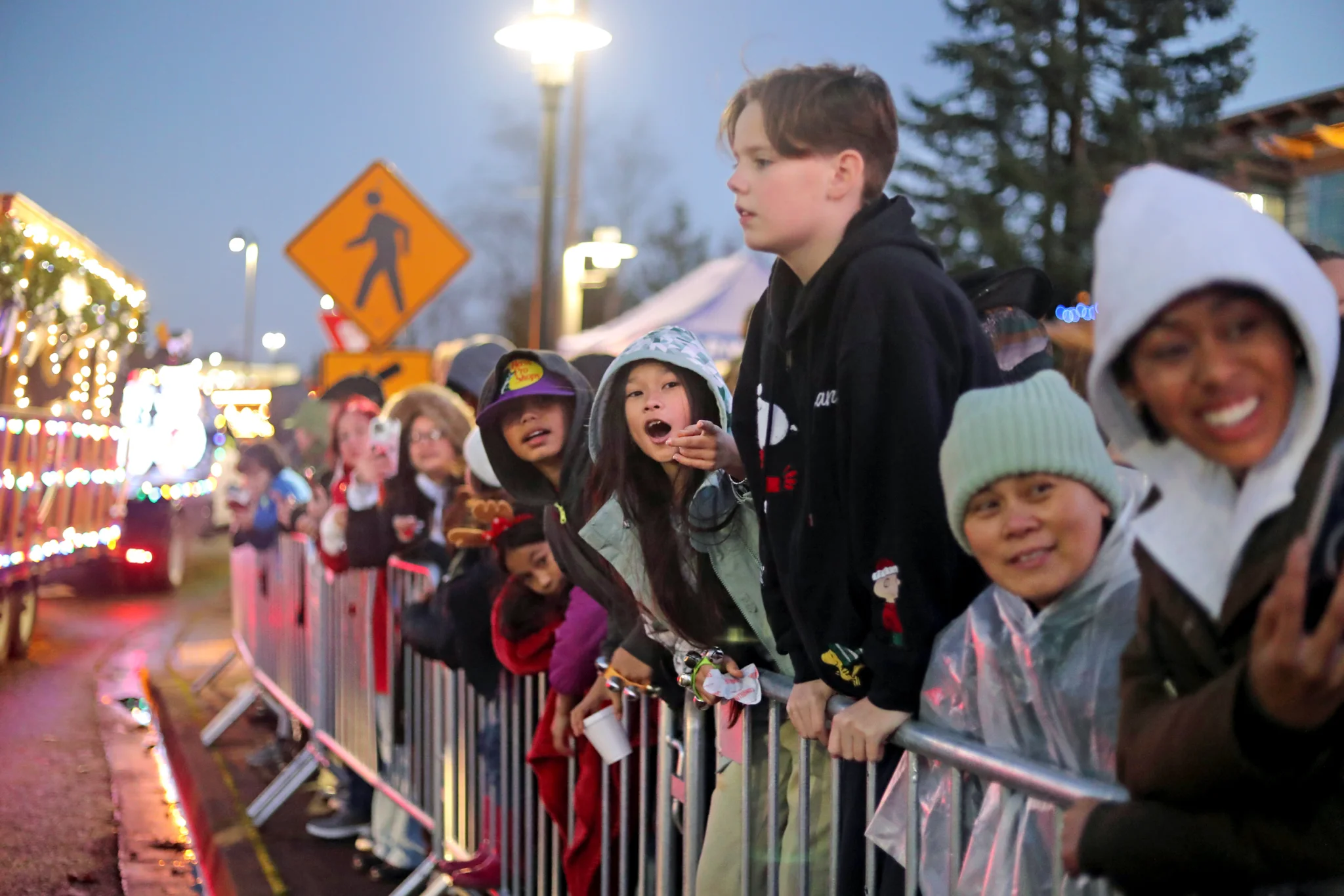 Kids lined up on a barrier rail observing a holiday parade.